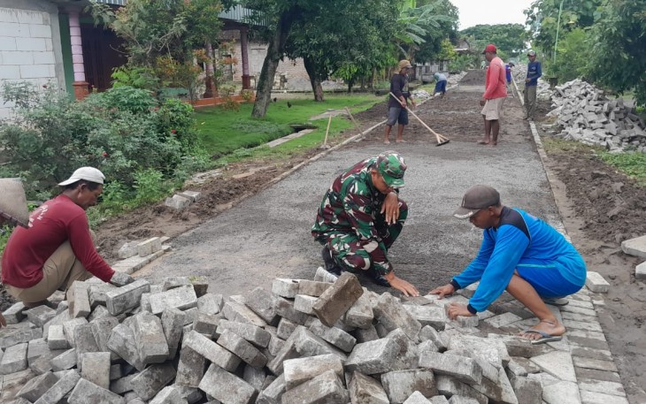 , Anggota Koramil 01/Ngawi Kodim 0805/Ngawi Serda Arif bersama-sama masyarakat melaksanakan kerja bakti pemasangan paving di Desa Mangunharjo Kecamatan Ngawi Kota, Minggu (29/12/2024)