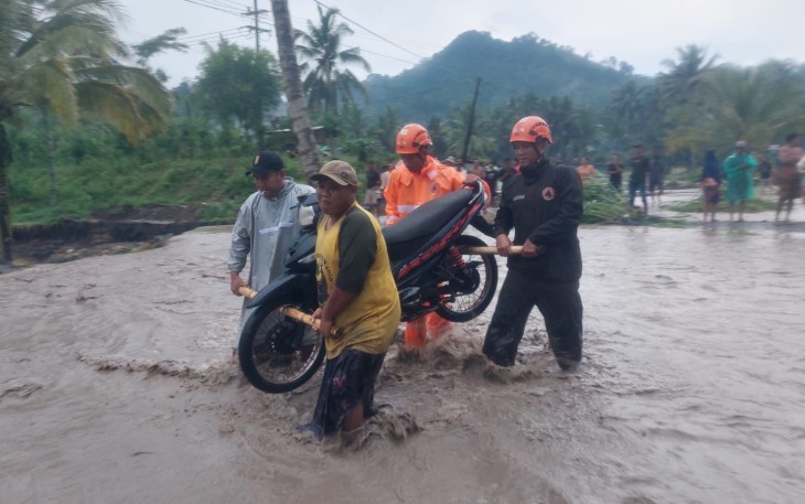 Petugas BPBD Kabupaten Lumajang saat membantu pengendara mengevakuasi motor yang terdampak banjir lahar dingin.