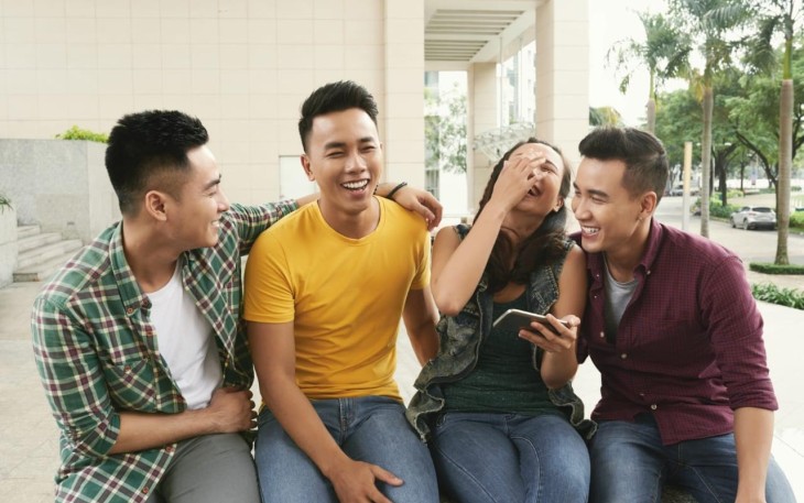 Foto Group of young Asian men and girl sitting together in urban street and laughing (Freepik.com)