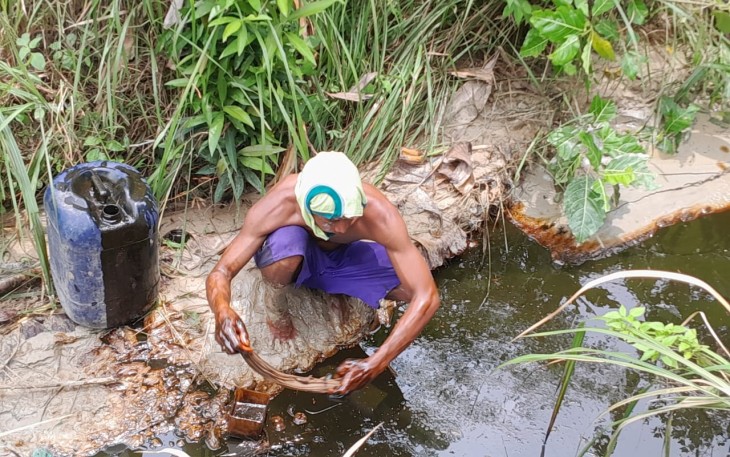 Salah satu warga Kedinding bernama Yanto sedang mengambil tumpahan minyak mentah yang mengalir ke sungai dengan cara manual atau istilahnya di pluntur.