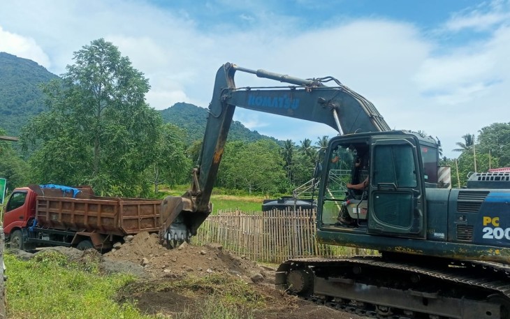 Foto satgas TMMD Kodim 1310/Bitung dengan menggunakan excavator melakukan pemerataan material pengerjaan pengerasan jalan