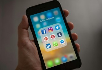 Ilustrasi tangan menggenggam handphone dengan layar yang  menampilkan platform media sosial.  Foto: Pexels/Tracy Le Blanc