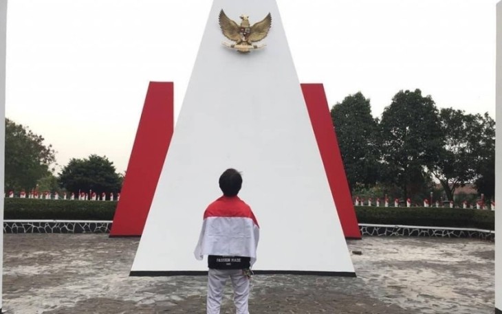Seorang Pria diselimuti Bendera Merah Putih Berdiri di depan Monumen Taman Makam Pahlawan Seribu Serpong, Tangerang Selatan, Kamis (15/8/2019). Foto: Adhimas Kevin