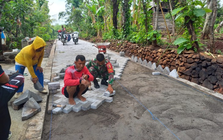  Anggota Koramil Kendal Kodim 0805/Ngawi Serma Simin bersama warga melaksanakan karya bakti gotong royong saling bahu membahu memasang paving blok jalan yang berada di Desa Kendal Kecamatan Kendal, Jum'at (11/04/2025)
