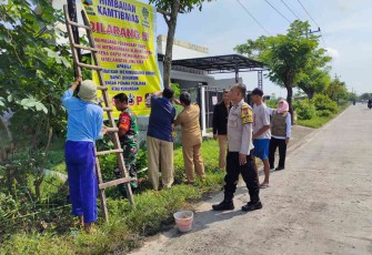 Serda Sutrisno bersama warga pasang banner di jalan desa