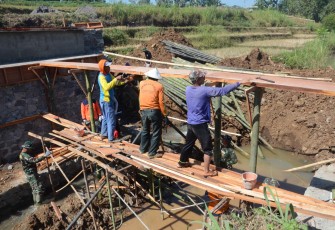 "Warga Mojogedang bersama Satgas TMMD Reg sedang memasang papan cor jembatan"