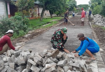 , Anggota Koramil 01/Ngawi Kodim 0805/Ngawi Serda Arif bersama-sama masyarakat melaksanakan kerja bakti pemasangan paving di Desa Mangunharjo Kecamatan Ngawi Kota, Minggu (29/12/2024)