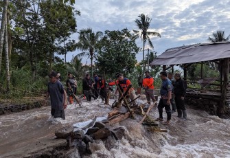 Tim gabungan membersihkan material kayu yang menyumbat jembatan desa akibat banjir bandang menerjang Desa Gunungsari, Kabupaten Bondowoso